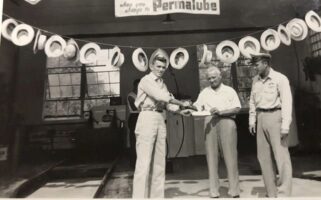 Historic photo of three men at a Permalube promotional display