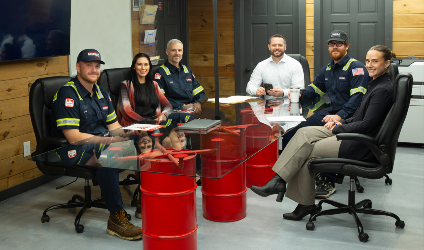 Kimbro team meeting around a table built on red oil drums